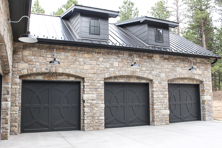 Modern Chateau Farmhouse style home with gooseneck lighting, black metal roof and custom european stone