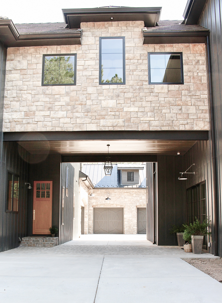 Modern Chateau Farmhouse exterior with stone, porte-cochere, and dark board and batten siding