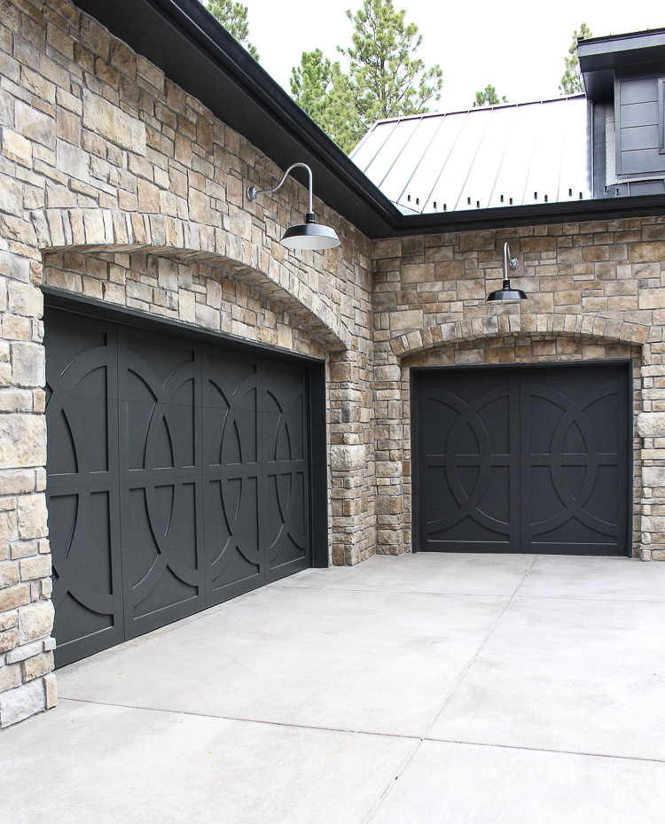 Modern Chateau Farmhouse exterior with custom european stone, porte-cochere, dark board and batten siding black metal roof