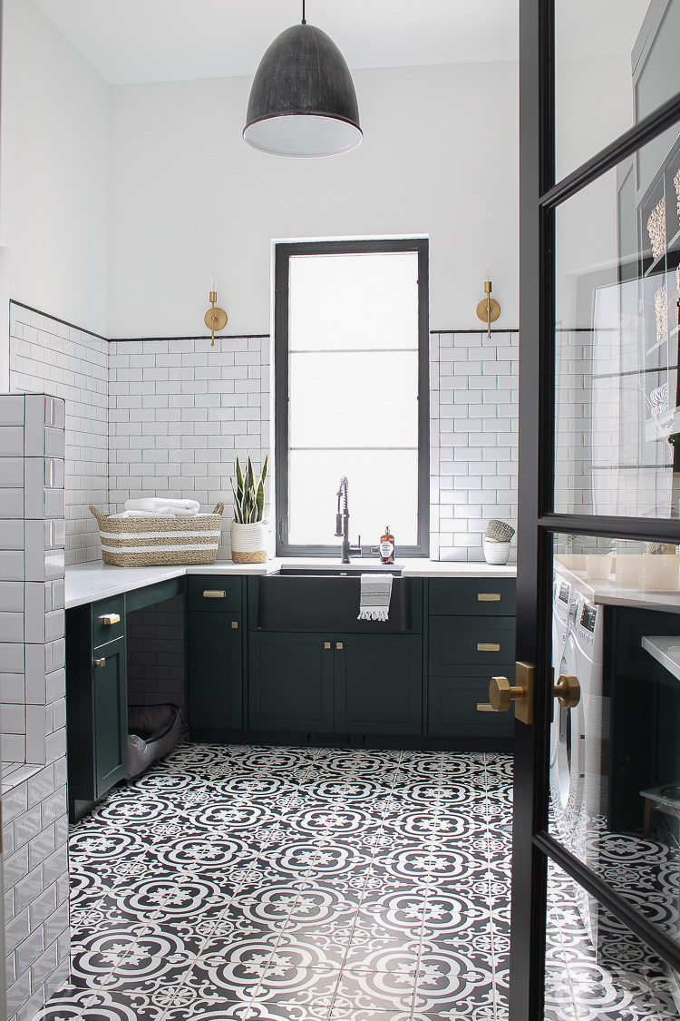 https://thehouseofsilverlining.com/wp-content/uploads/2019/02/black-white-laundry-room-beveled-subway-tile-patterned-floor-dark-green-cabinets-natural-wood-gold-hardware.jpg